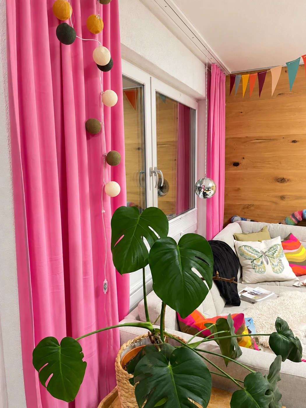 Pinke Vorhänge an einem grossen Fenster mit Holzvertäfelung und Zimmerpflanze